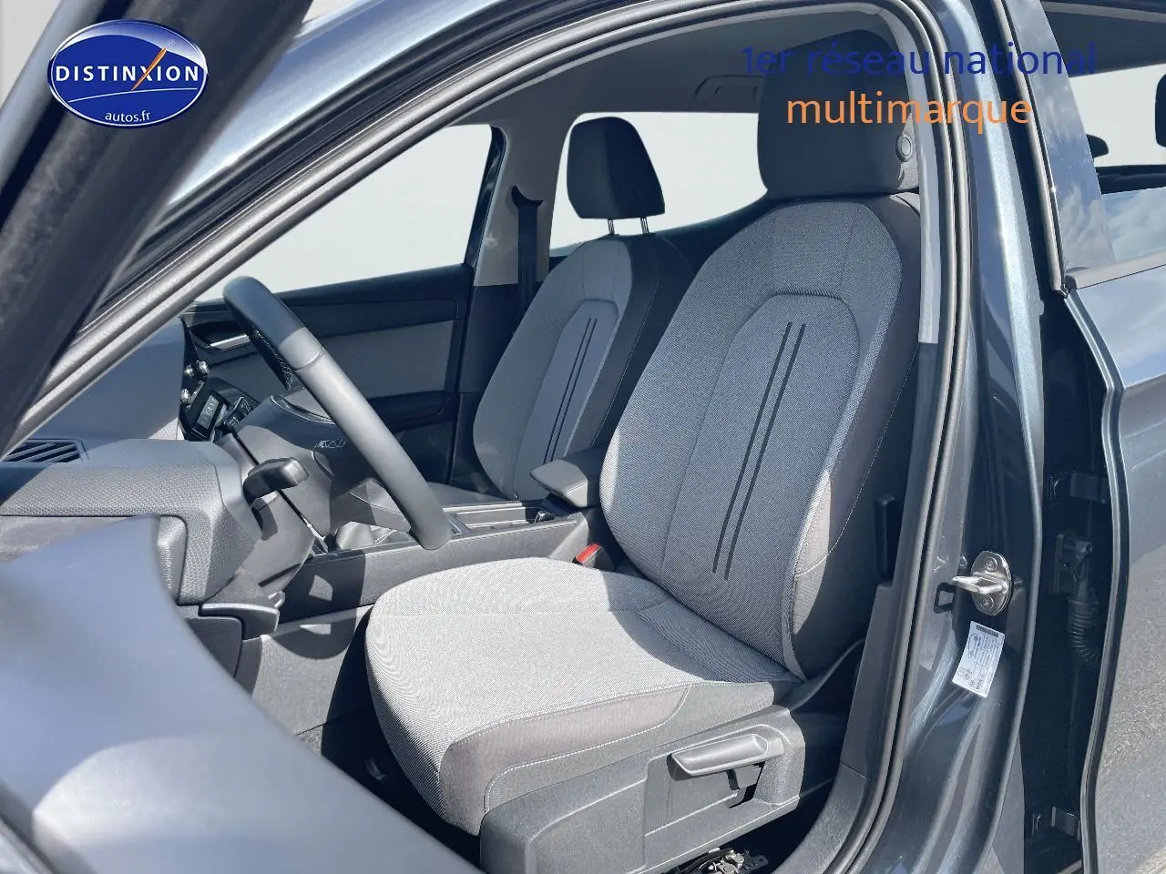 Vue intérieure côté conducteur de la SEAT LEON IV gris magnétique, mettant en valeur les sièges en tissu gris clair.