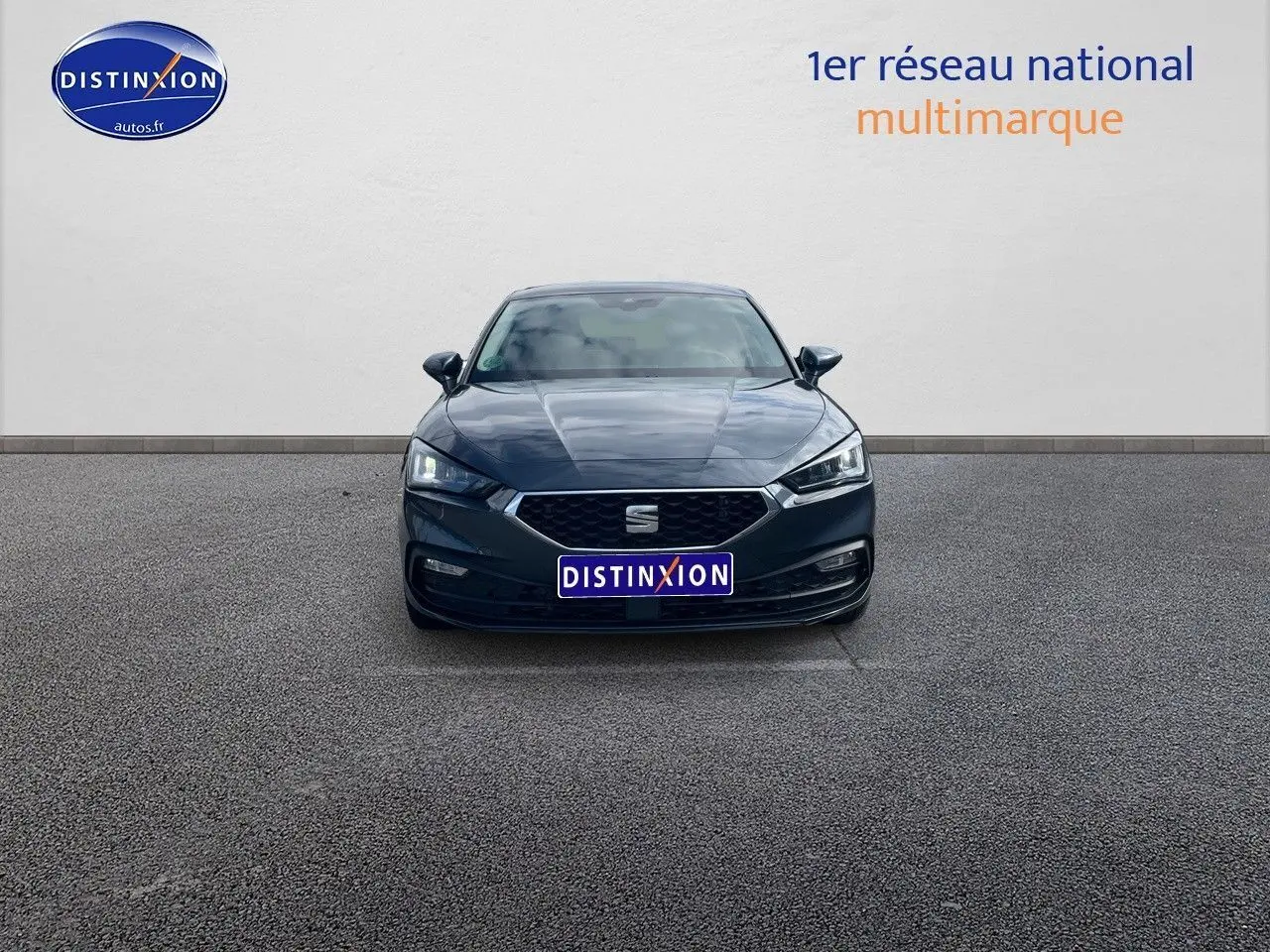 Vue frontale d'une SEAT Leon IV gris magnétique métal avec calandre hexagonale et phares LED allumés.