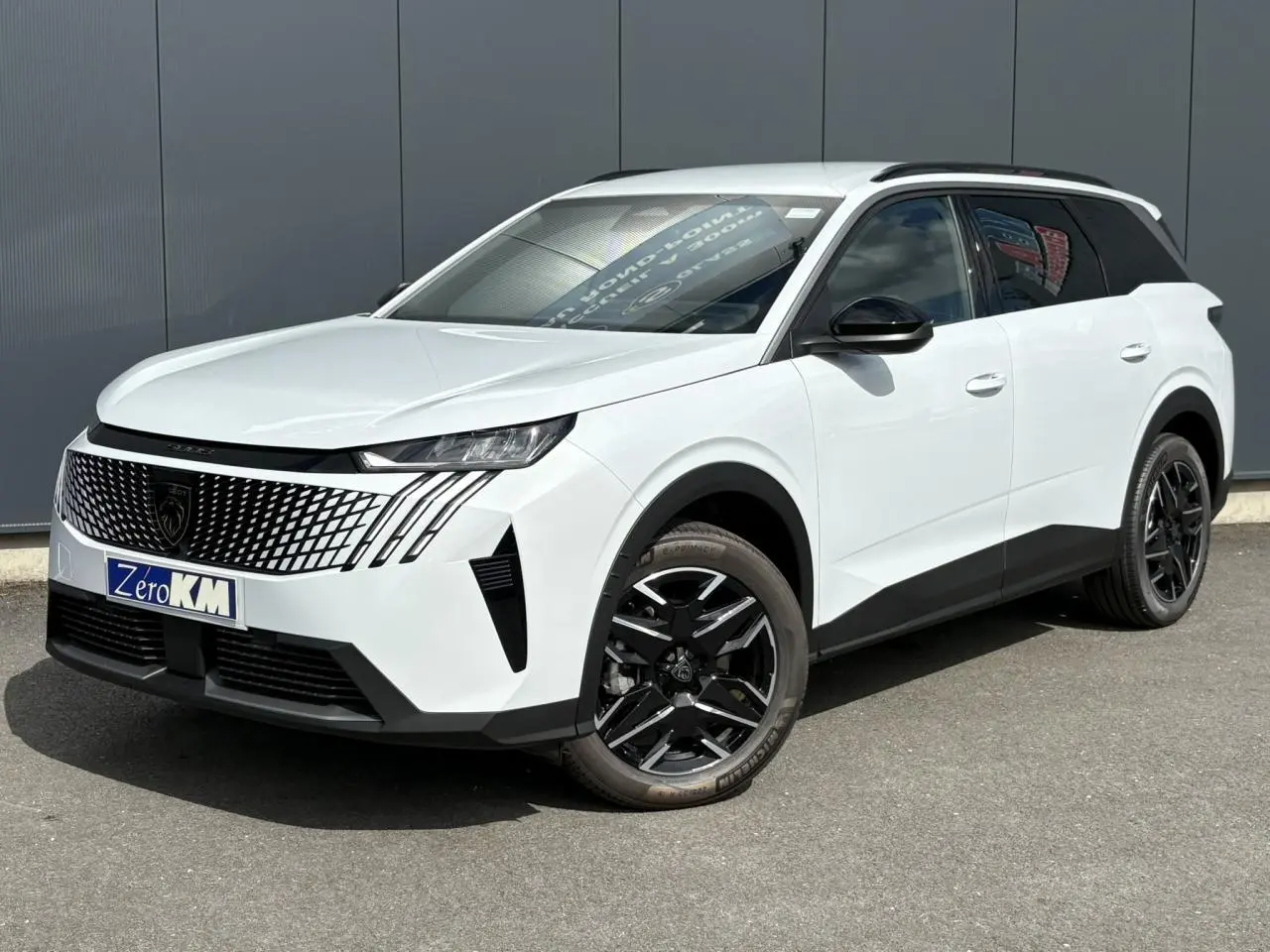 Peugeot 5008 Hybrid blanc Okénite vu de 3/4 avant droit avec jantes noires et barres de toit noires.