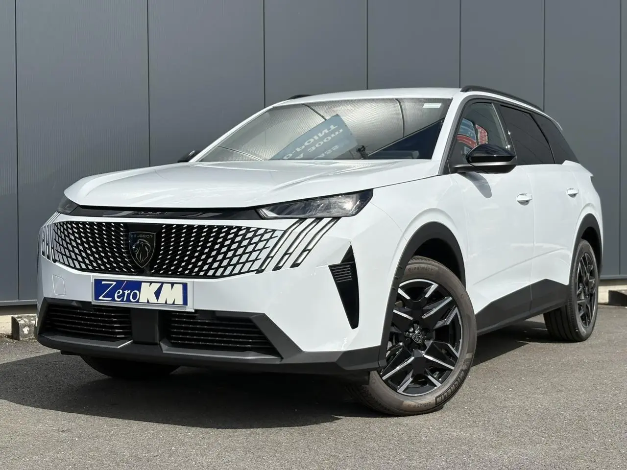 Peugeot 5008 blanc Okénite en 3/4 avant droit, avec calandre noire distinctive et jantes alliage noires.