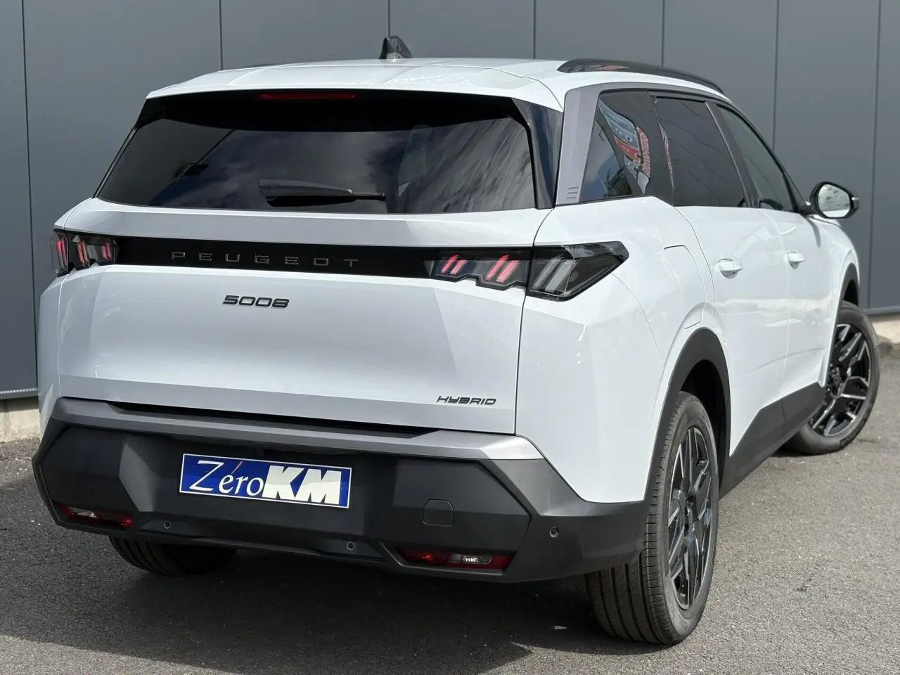 Vue 3/4 arrière droite d'un Peugeot 5008 Hybrid blanc Okénite avec feux arrière LED 3 griffes et jantes alliage noires.