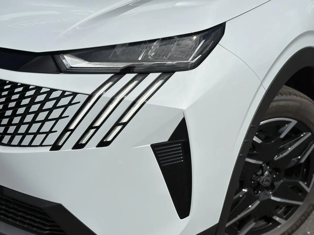 Gros plan sur l'avant droit blanc Okénite du Peugeot 5008 Hybrid 2025, mettant en valeur les feux LED griffés et la jante noire.