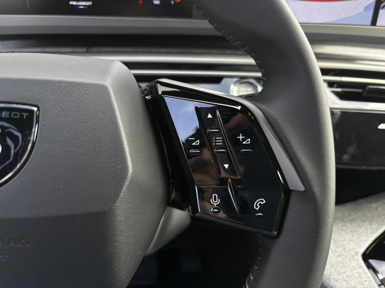 Gros plan sur les commandes noires du volant cuir du Peugeot 5008 Hybrid blanc Okénite, intérieur moderne et épuré.