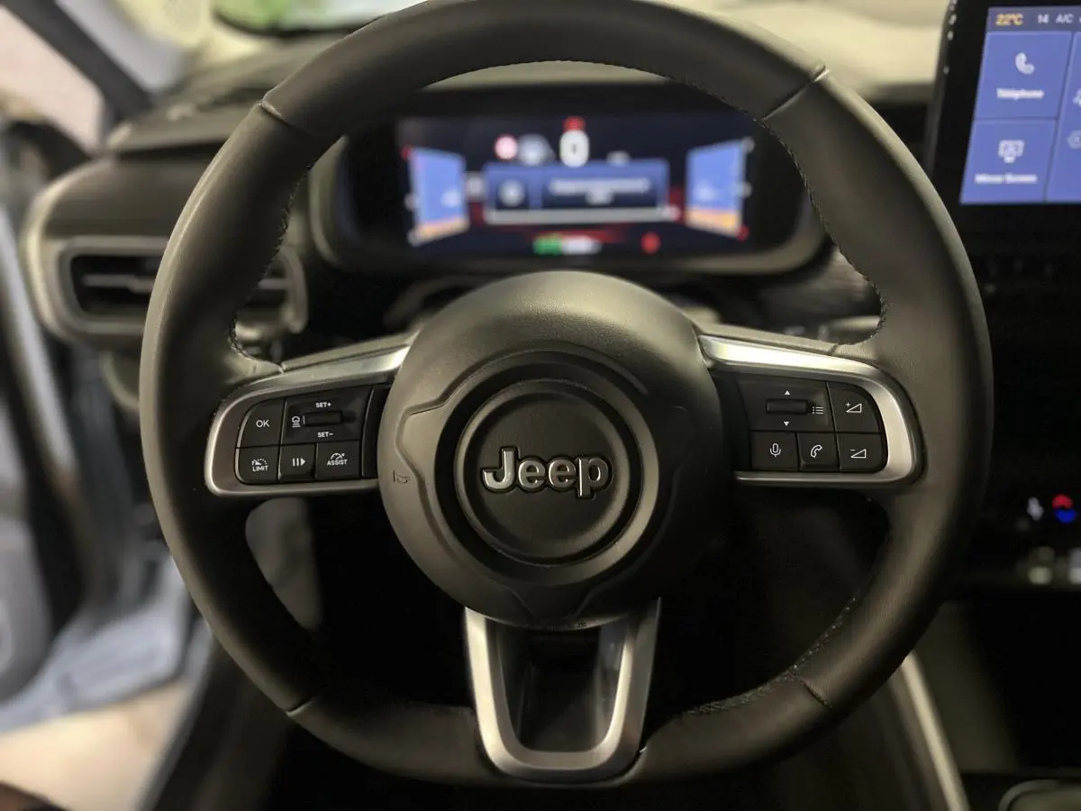 Gros plan sur le volant noir du Jeep Avenger 2024 avec commandes intégrées et tableau de bord numérique flou en arrière-plan.