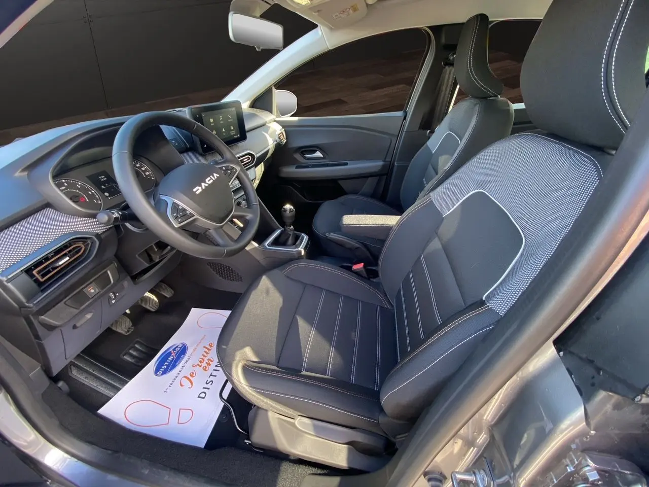 Intérieur côté conducteur de la Dacia Sandero Stepway gris schiste, volant multifonction et sièges tissu noir avec surpiqûres.