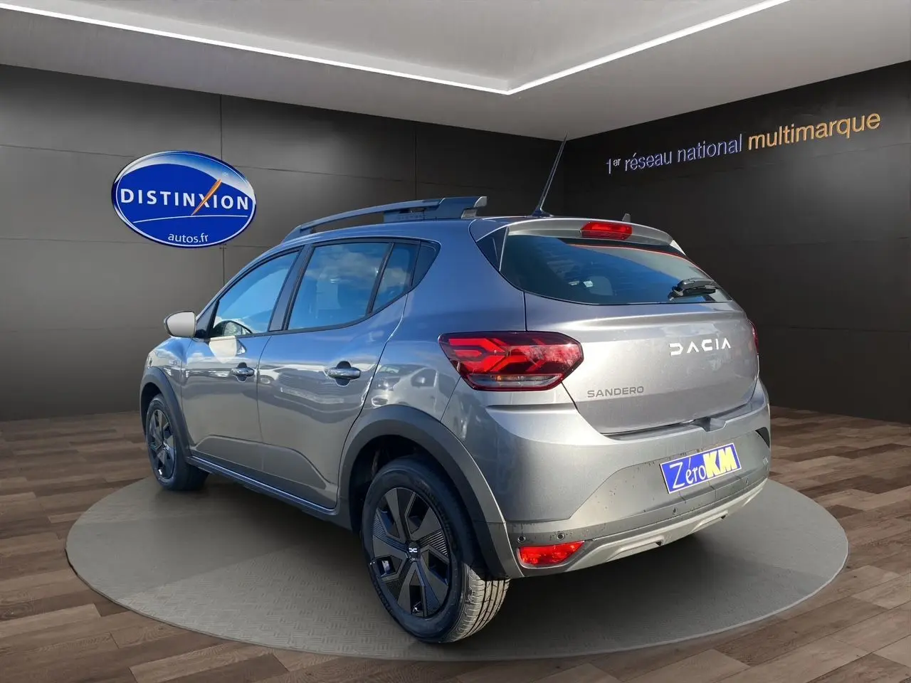 Vue 3/4 arrière droite d'une Dacia Sandero Stepway gris schiste avec barres de toit et jantes noires en showroom.