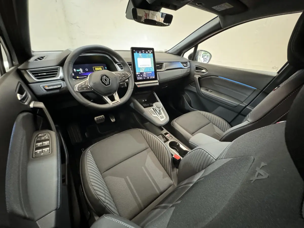 Vue intérieure côté conducteur du Renault Captur esprit Alpine E-Tech 2025, sièges noirs et écran tactile vertical central.
