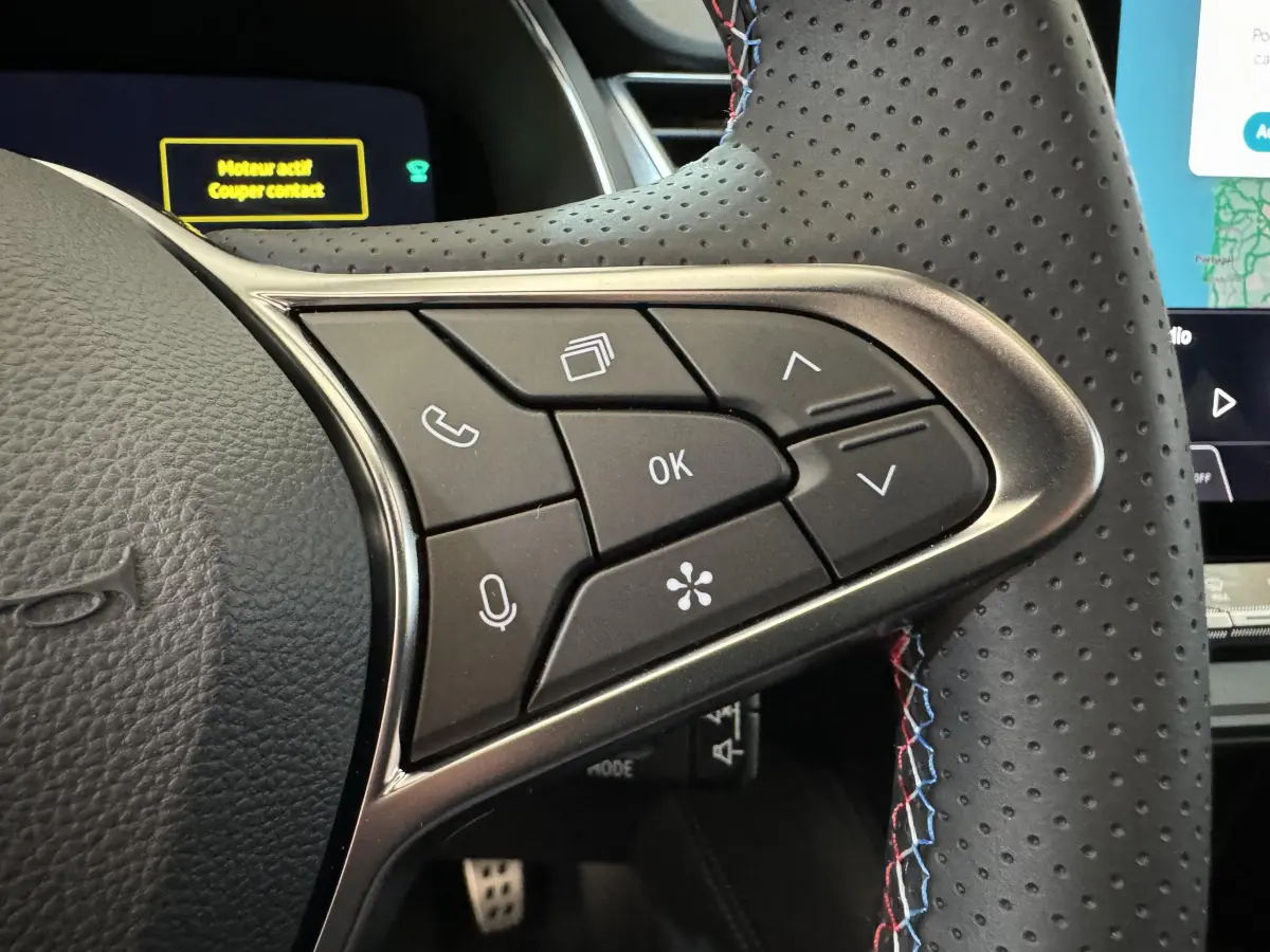 Gros plan sur les commandes multifonctions du volant perforé avec surpiqûres tricolores du Renault Captur blanc esprit Alpine E-Tech.