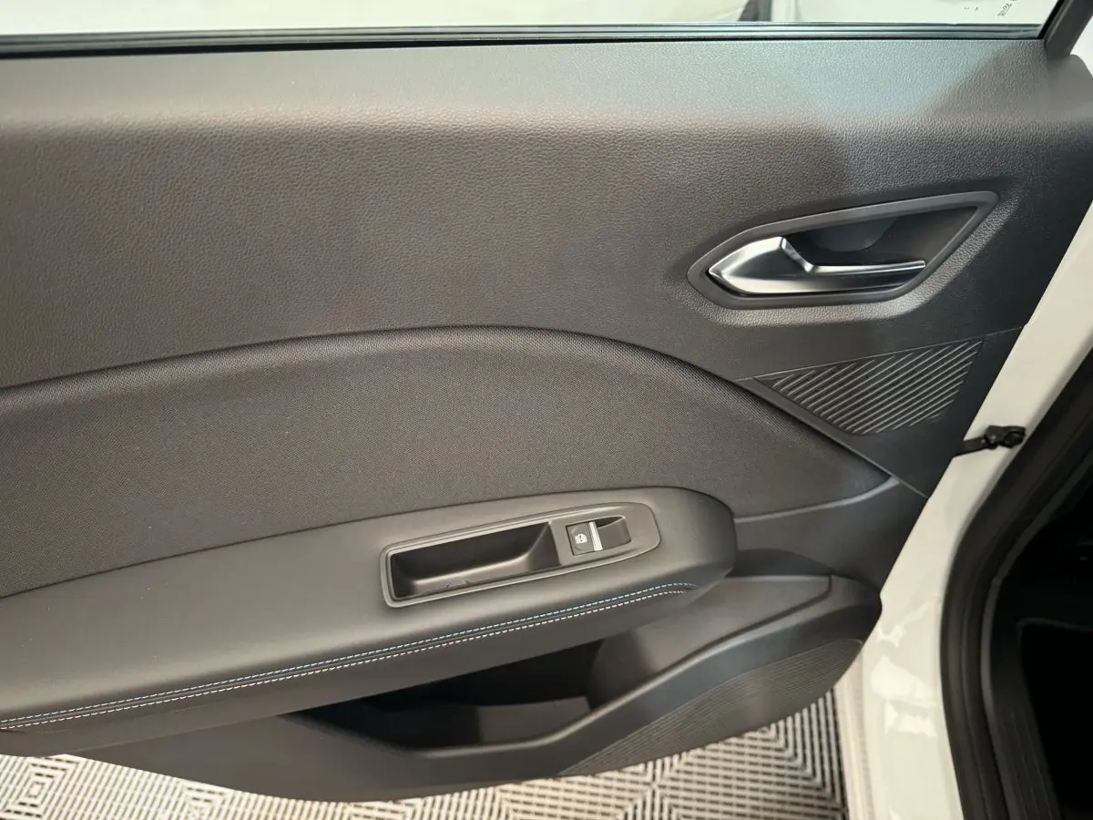 Gros plan sur la porte intérieure côté gauche du Renault Captur blanc, avec surpiqûres bleues et bouton de verrouillage.