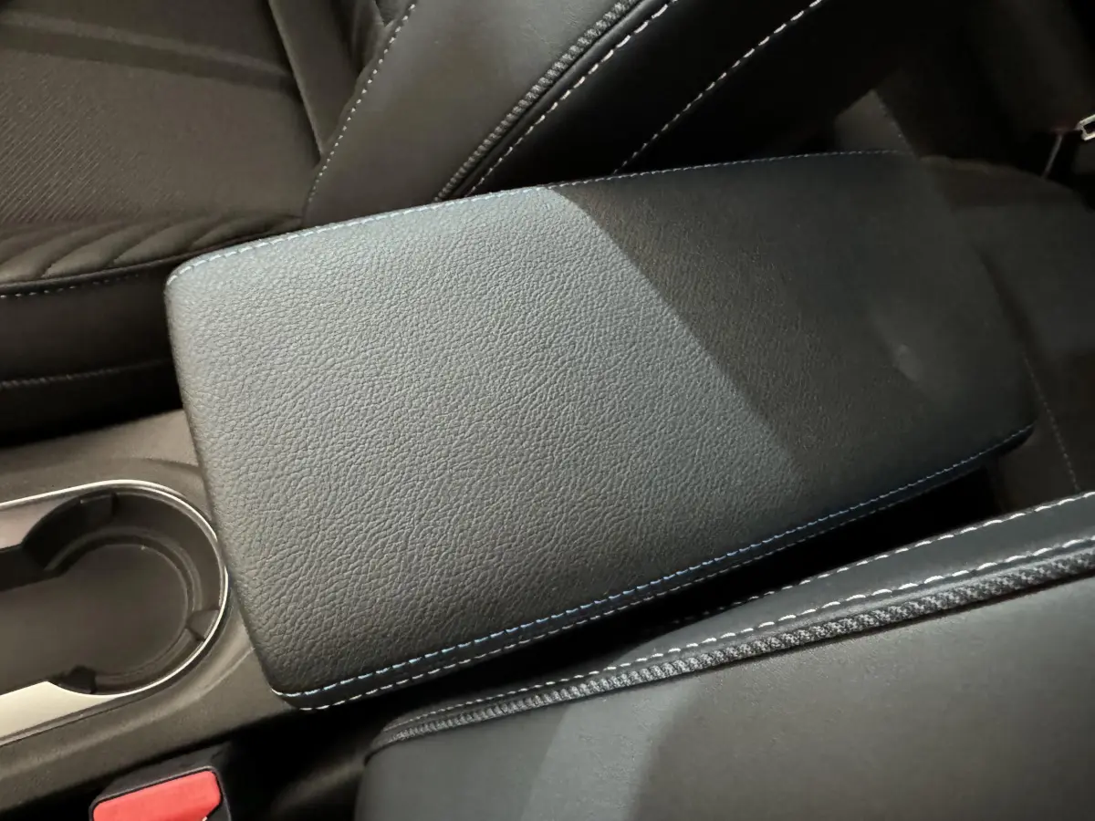 Gros plan sur l'accoudoir central noir avec surpiqûres bleues dans l'habitacle du Renault Captur blanc esprit Alpine E-Tech.