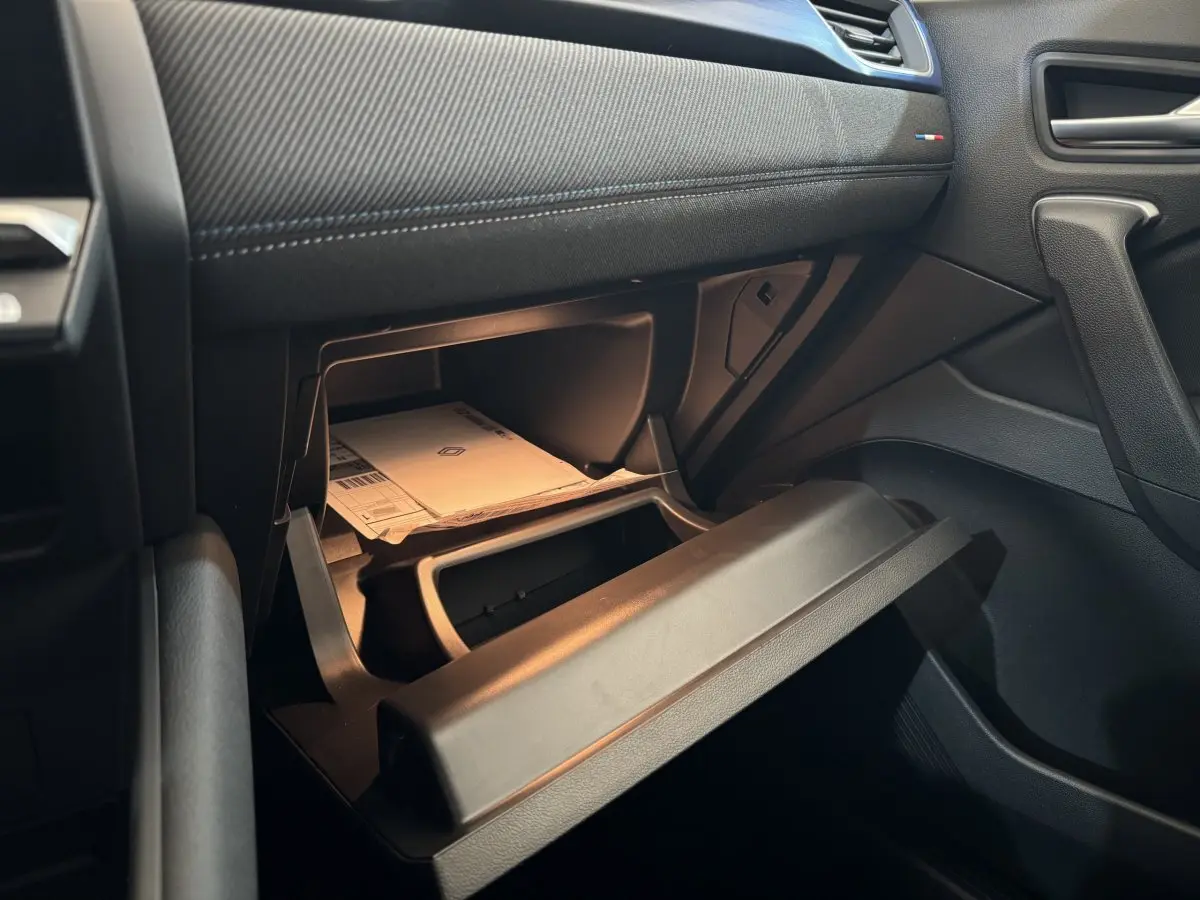 Vue intérieure côté passager du coffre à gants ouvert du Renault Captur blanc esprit Alpine E-Tech 2025 avec documents visibles.