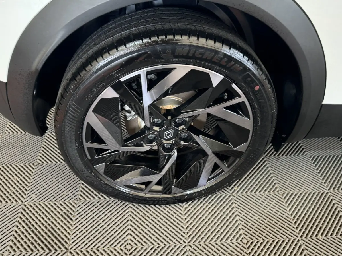 Gros plan sur la roue avant droite du Renault Captur blanc esprit Alpine E-Tech, jante alliage noire et argentée au design géométrique.