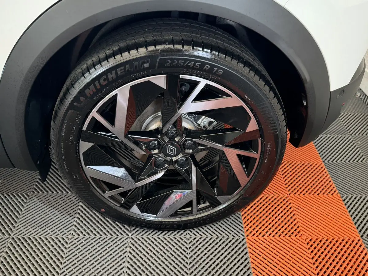 Gros plan sur la roue avant droite du Renault Captur blanc, mettant en valeur la jante noire et argentée au design géométrique.