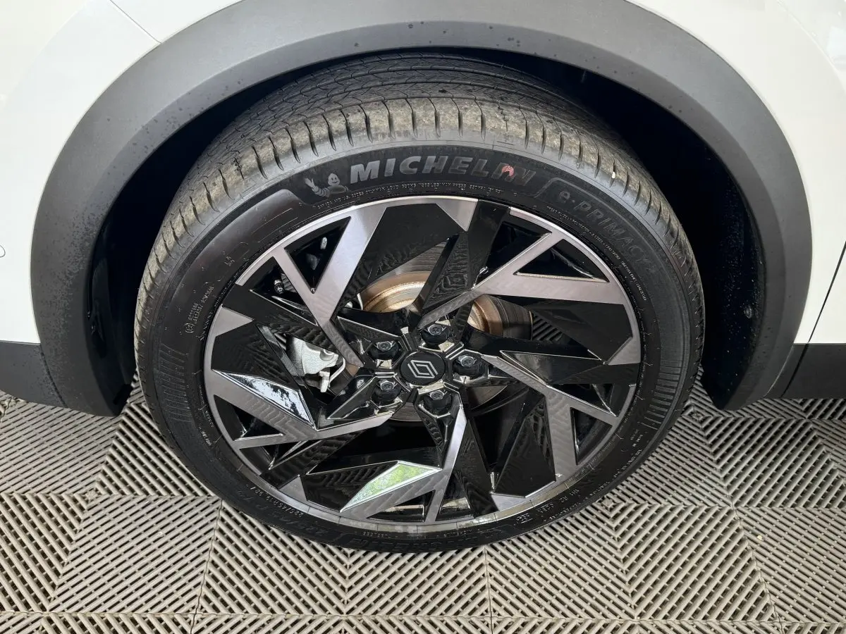 Gros plan sur la roue avant droite du Renault Captur blanc esprit Alpine avec jante noire et argentée au design géométrique.