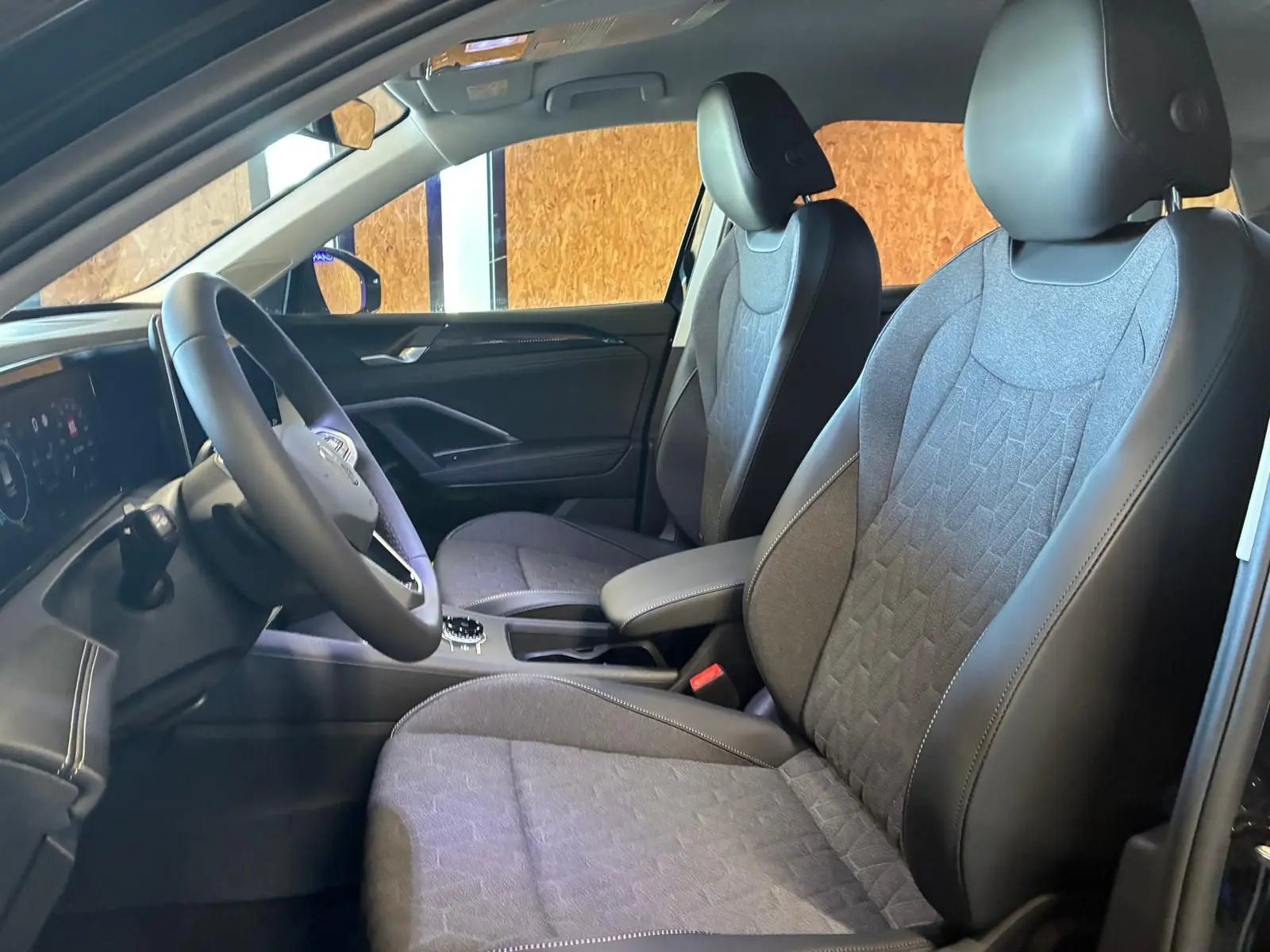 Vue intérieure côté gauche du Volkswagen Tiguan 2026, sièges tissu gris avec contours cuir noir et volant multifonction.