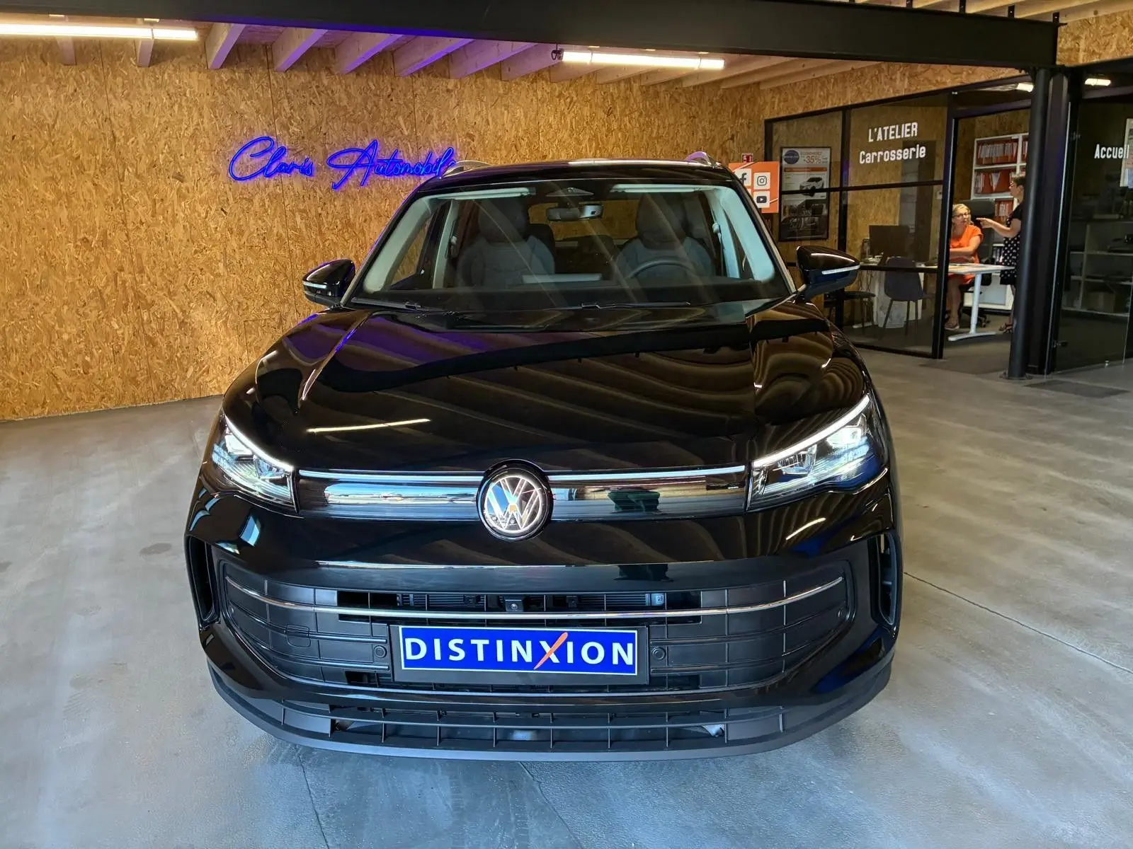 Vue avant d'un Volkswagen Tiguan noir grenadilla métallisé, avec calandre chromée et plaques Distinxion en intérieur showroom.