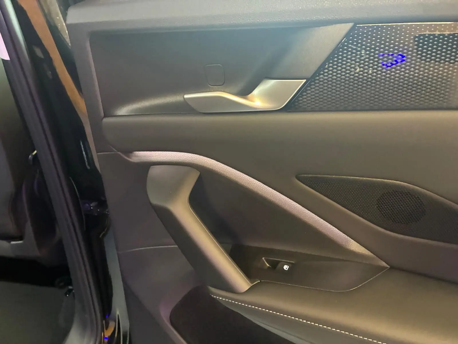 Gros plan sur la porte intérieure côté gauche du Volkswagen Tiguan noir avec poignée argentée et éclairage d’ambiance bleu.