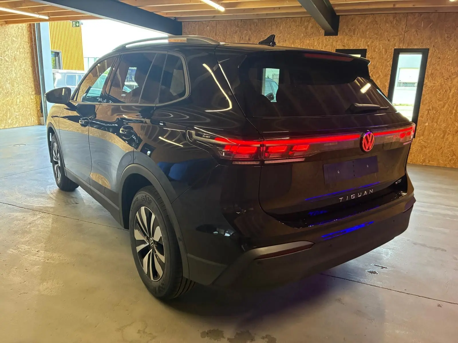 Vue 3/4 arrière droite du Volkswagen Tiguan noir Grenadilla avec feux arrière LED allumés en intérieur.