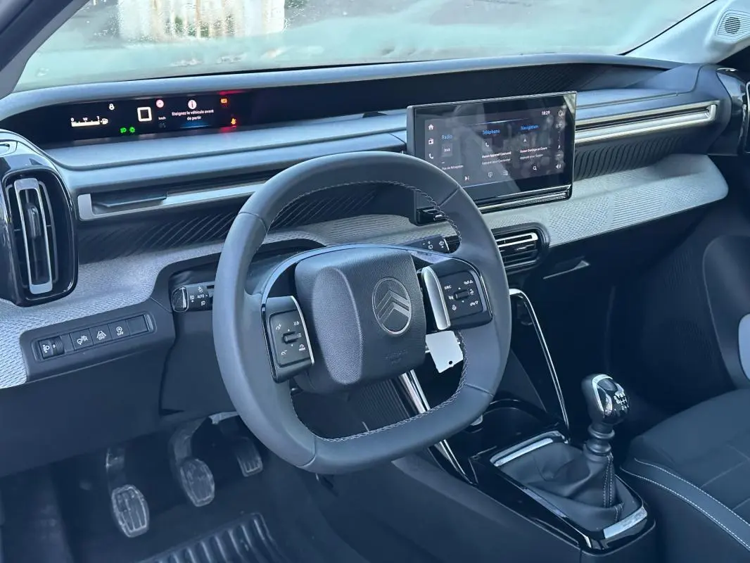 Vue intérieure avant de la Citroën C3 2025 noire, volant multifonction, écran tactile et levier de vitesse manuel visibles.