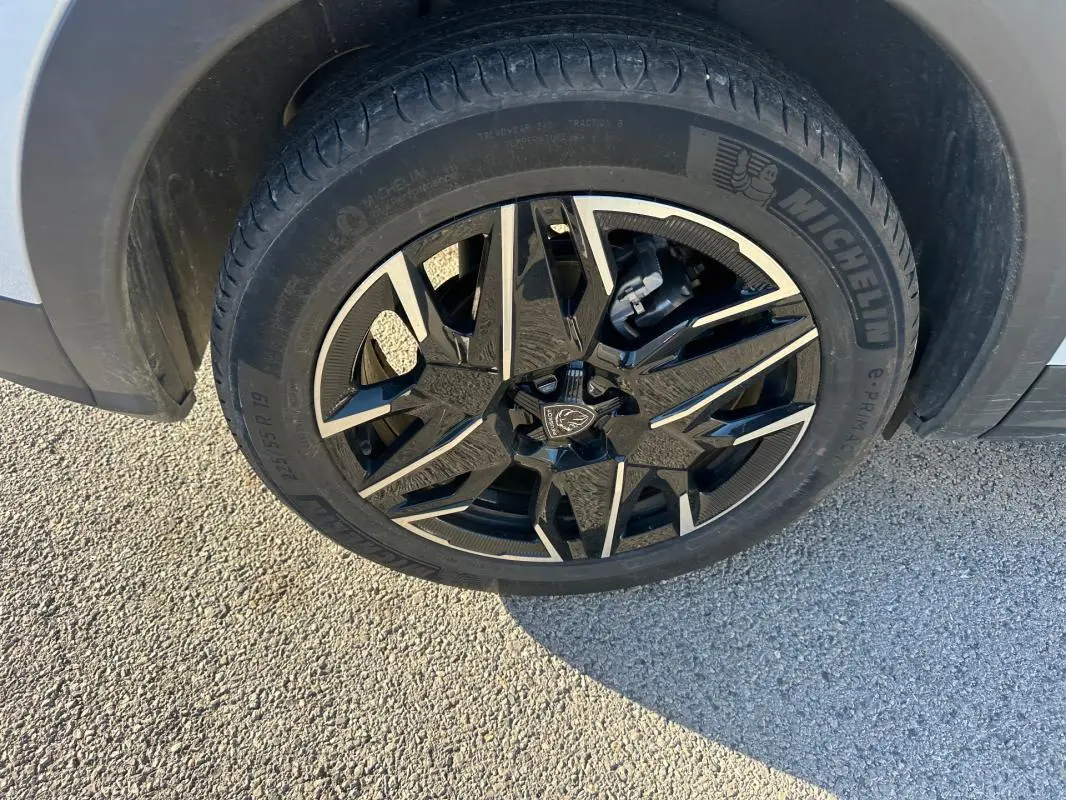 Gros plan sur la jante alliage noire et argent 19 pouces du côté avant droit du Peugeot 3008 blanc Hybrid 145 e-DCS6 Allure.