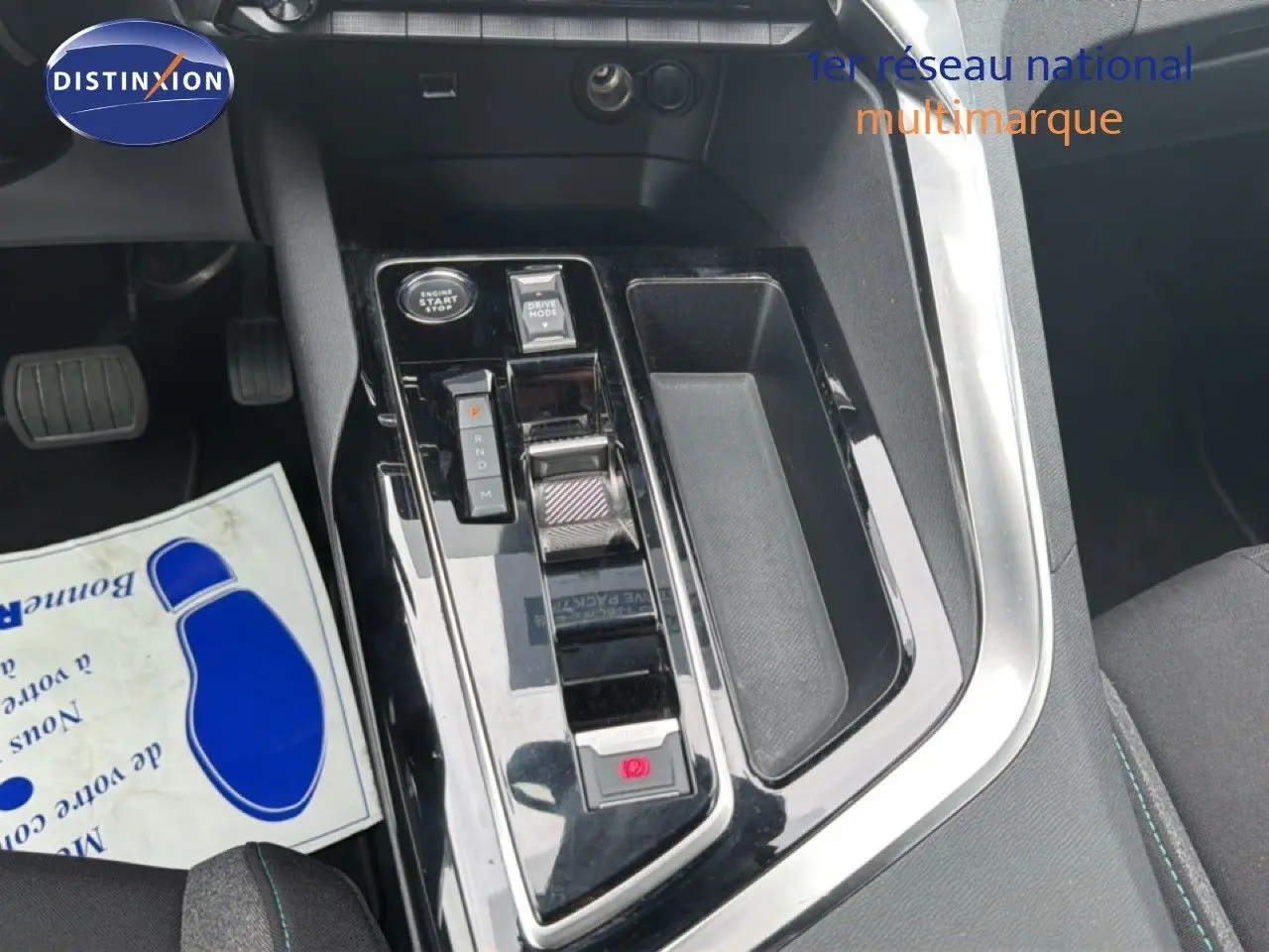 Gros plan sur la console centrale noire brillante du Peugeot 5008 bleu Celebes, avec levier de vitesses automatique et bouton start.