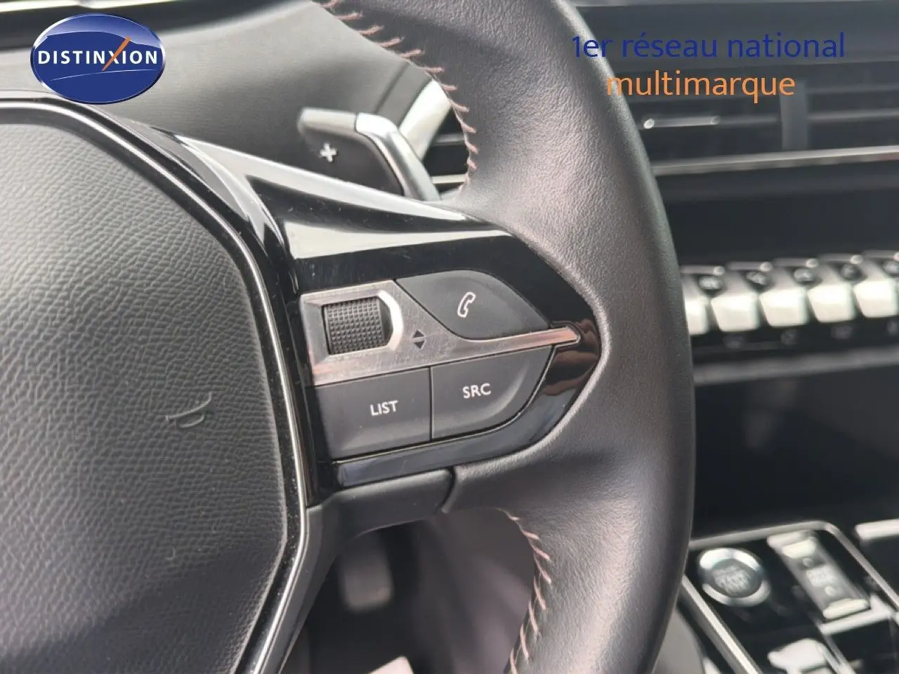 Gros plan sur le volant cuir noir du Peugeot 5008 bleu Célèbes, avec commandes intégrées et tableau de bord en arrière-plan.