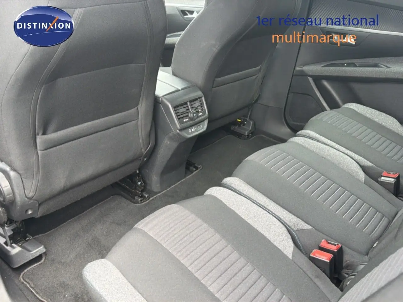 Vue intérieure arrière du Peugeot 5008 Hybrid 2024 montrant les sièges tissu gris et la console centrale avec aérateurs.