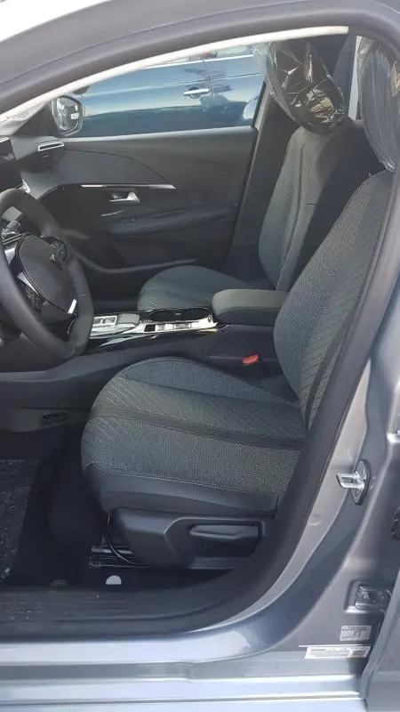 Vue intérieure côté conducteur de la Peugeot 208 Hybrid 110 gris, sièges tissu et volant réglable visibles.