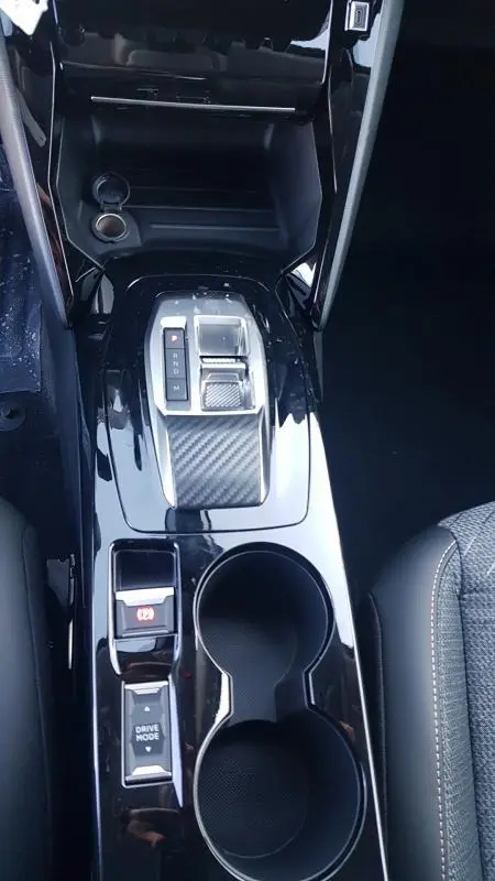 Vue plongeante sur la console centrale noire brillante de la Peugeot 208 Hybrid 110, avec levier de boîte auto et porte-gobelets.