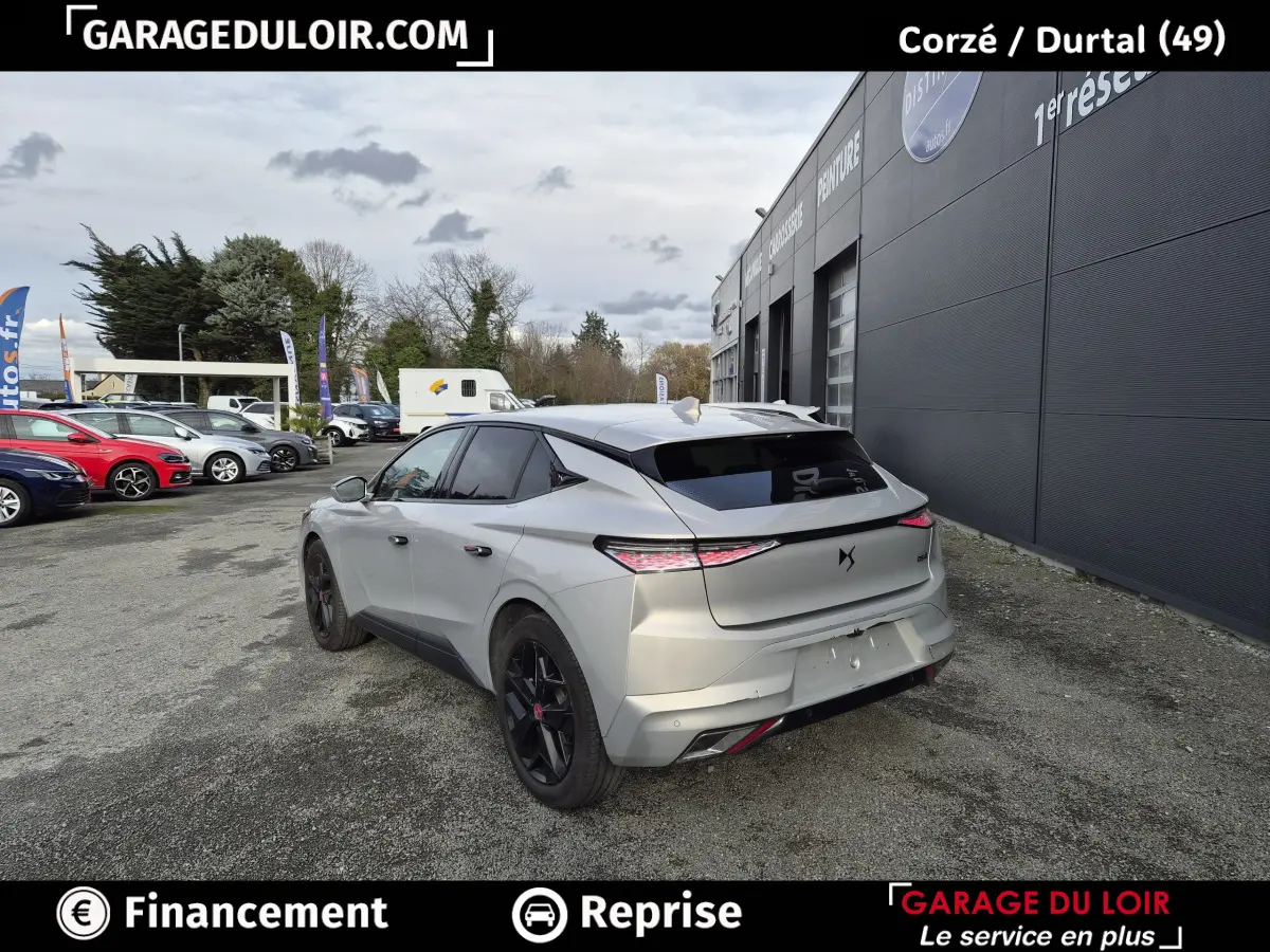 Vue 3/4 arrière droite d'une DS4 beige 2024 avec feux arrière LED et jantes noires, stationnée près d'un bâtiment gris.