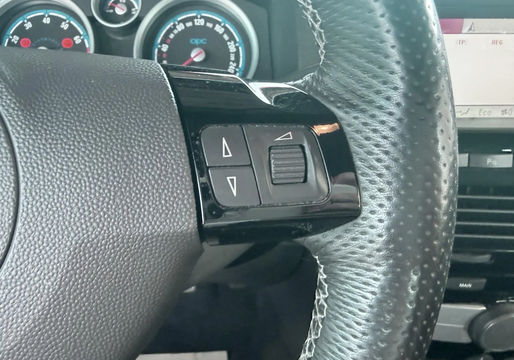 Gros plan sur le volant en cuir noir de l’Opel Astra OPC 2008 avec commandes intégrées et compteurs en arrière-plan.