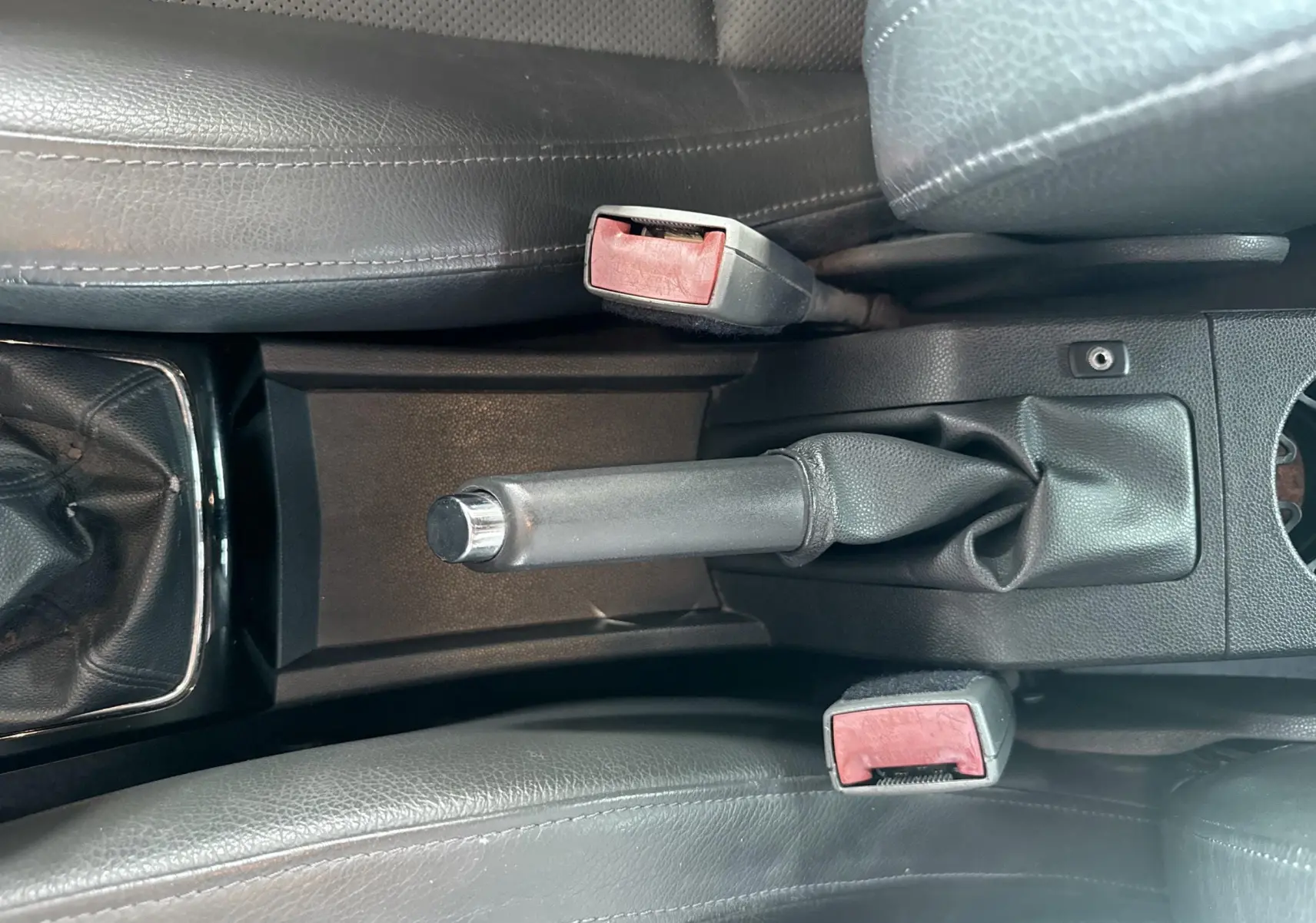 Vue rapprochée de la console centrale avec frein à main manuel et ceintures de sécurité rouges sur Opel Astra OPC 2008.