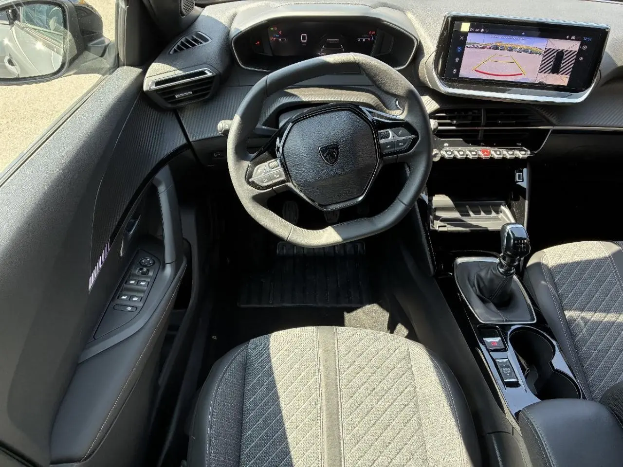 Vue intérieure du poste de conduite du Peugeot 2008 2024, volant compact, écran tactile avec caméra de recul, sellerie grise.