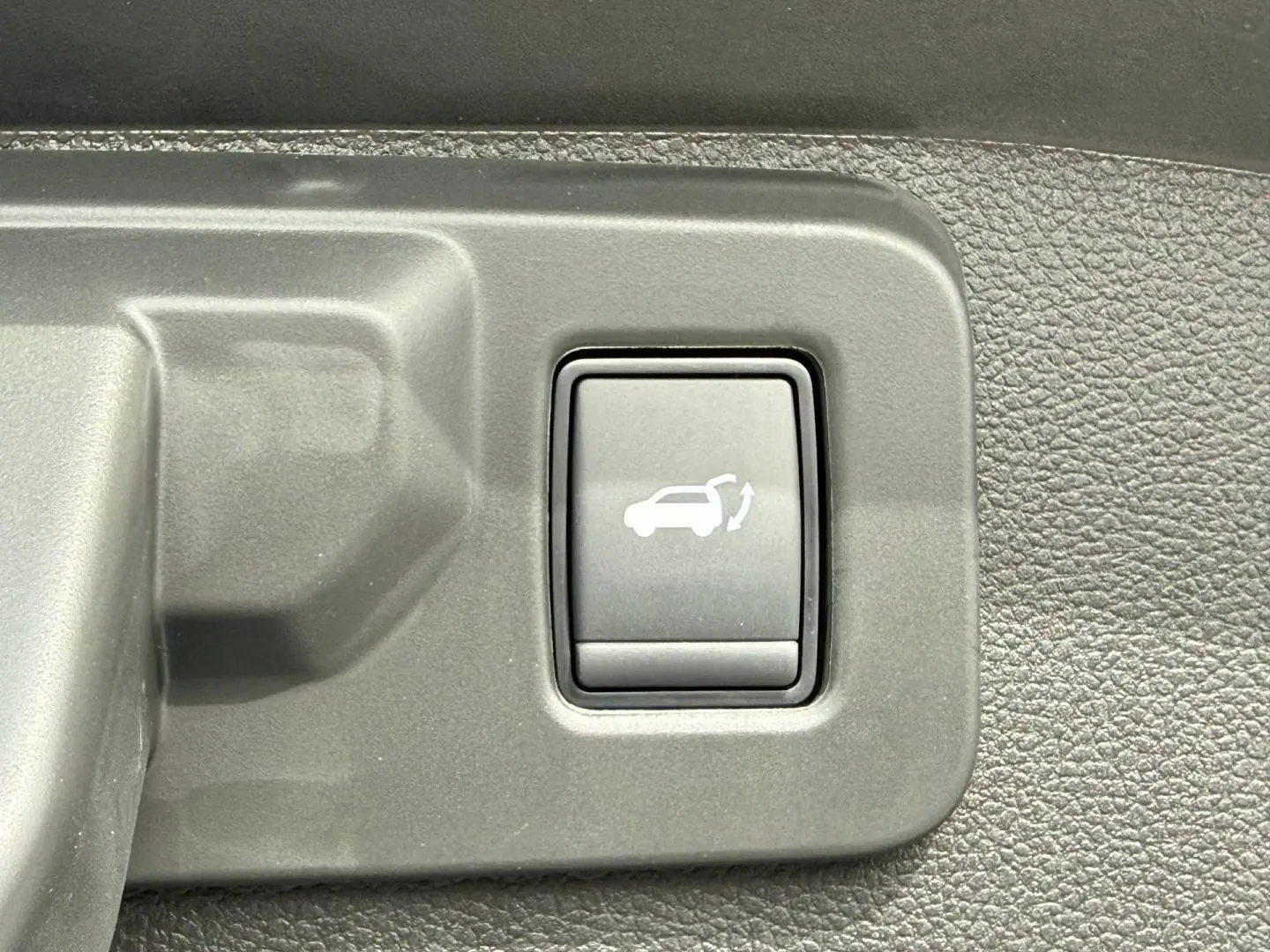 Gros plan sur le bouton d'ouverture électrique du coffre dans l'habitacle du Renault Austral gris Schiste satin.