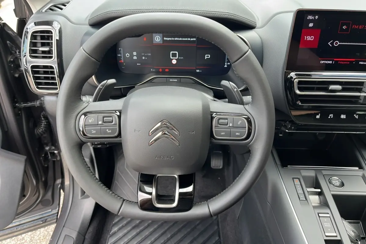 Vue intérieure centrée sur le volant multifonction du Citroën C5 Aircross Hybrid 2025 avec tableau de bord numérique.