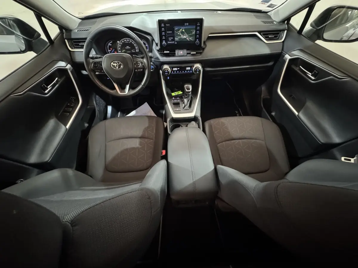 Vue intérieure avant du Toyota RAV4 hybride 2021 avec tableau de bord moderne, écran tactile et sièges noirs en tissu.