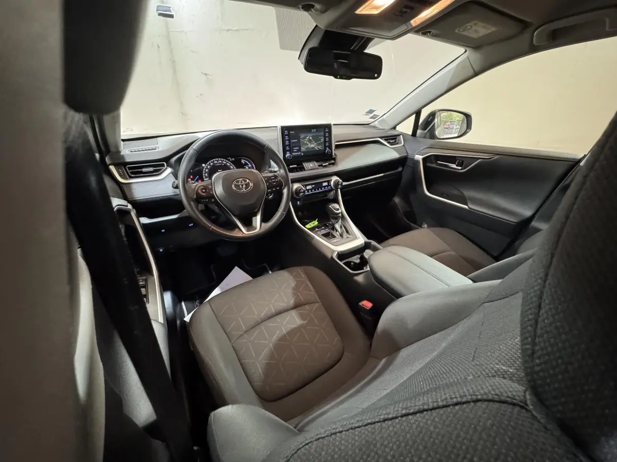 Intérieur Toyota RAV4 hybride 2021 vu côté conducteur, sièges noirs et tableau de bord avec écran tactile central.