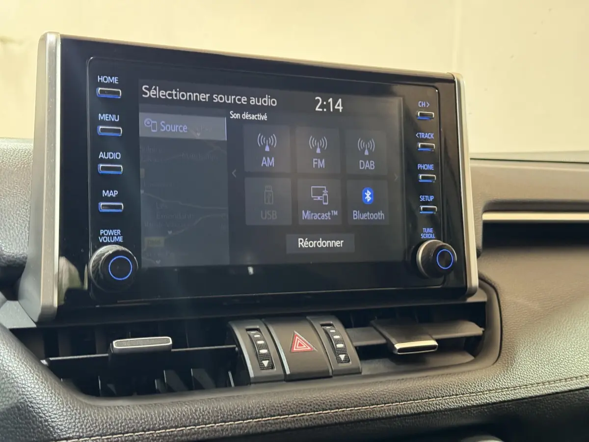 Écran tactile central du Toyota RAV4 hybride 2021, vue rapprochée du tableau de bord noir avec commandes audio visibles.