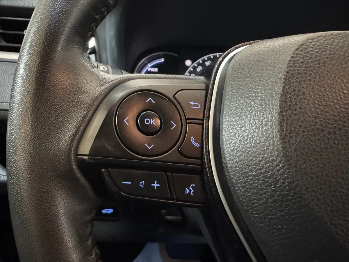 Gros plan sur les commandes du volant cuir noir du Toyota RAV4 hybride 2021, avec boutons rétroéclairés bleus.