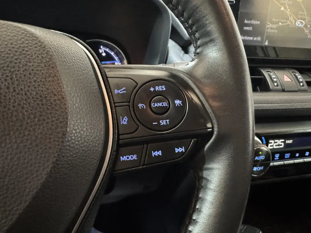 Gros plan sur le volant cuir noir côté droit du Toyota RAV4 hybride 2021 avec commandes de régulateur et multimédia éclairées.