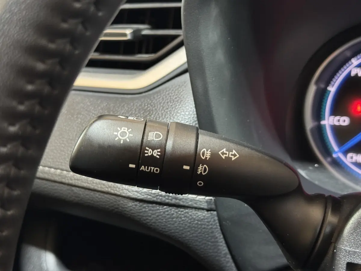 Gros plan sur la commande des feux à gauche du volant du Toyota RAV4 hybride gris clair, avec tableau de bord partiellement visible.