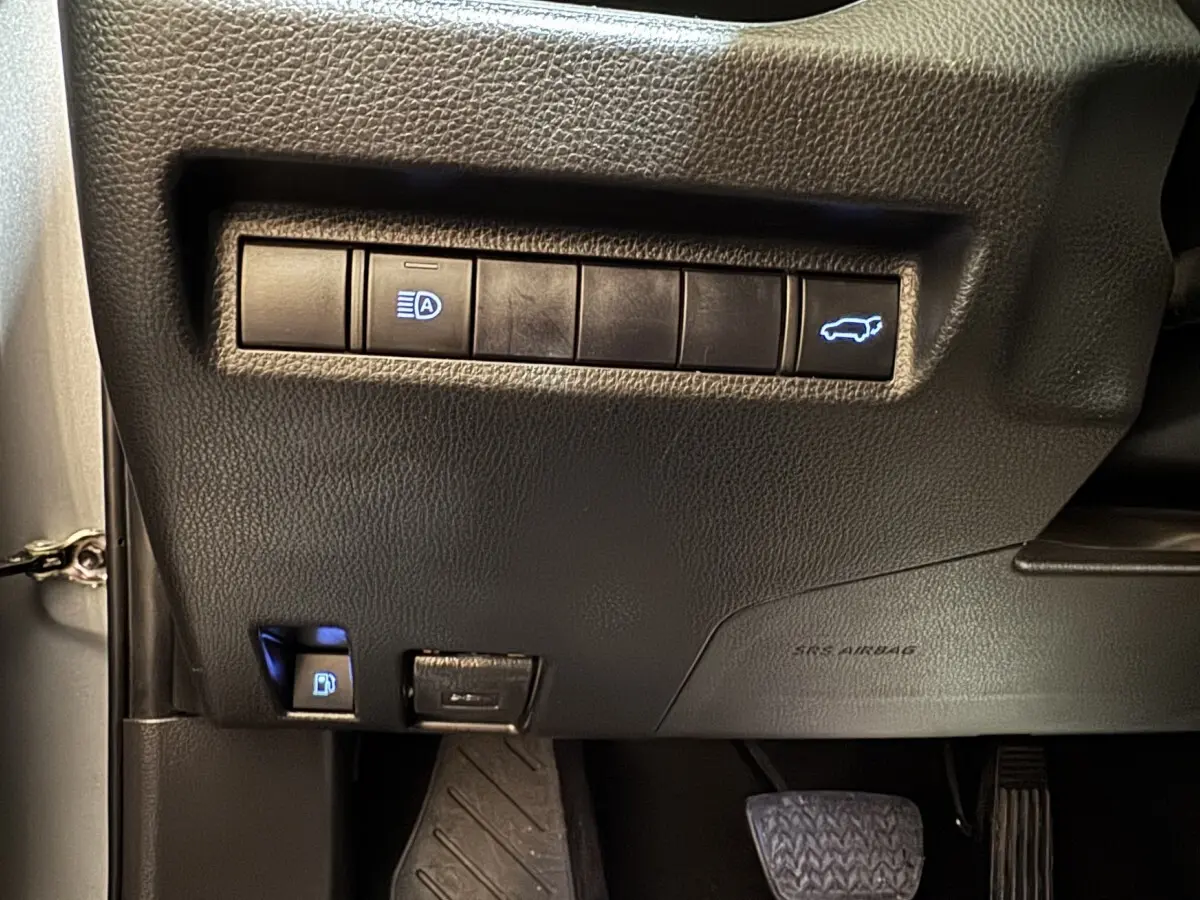 Gros plan sur les commandes noires sous le tableau de bord du Toyota RAV4 gris clair, avec bouton ouverture coffre éclairé.