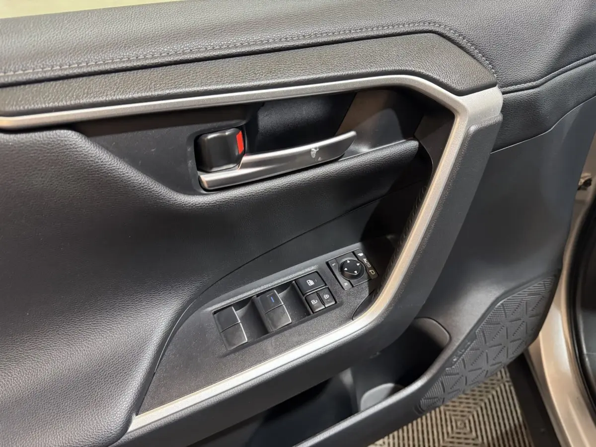 Gros plan sur la porte intérieure côté conducteur du Toyota RAV4 gris clair, avec commandes de vitres et rétroviseurs.
