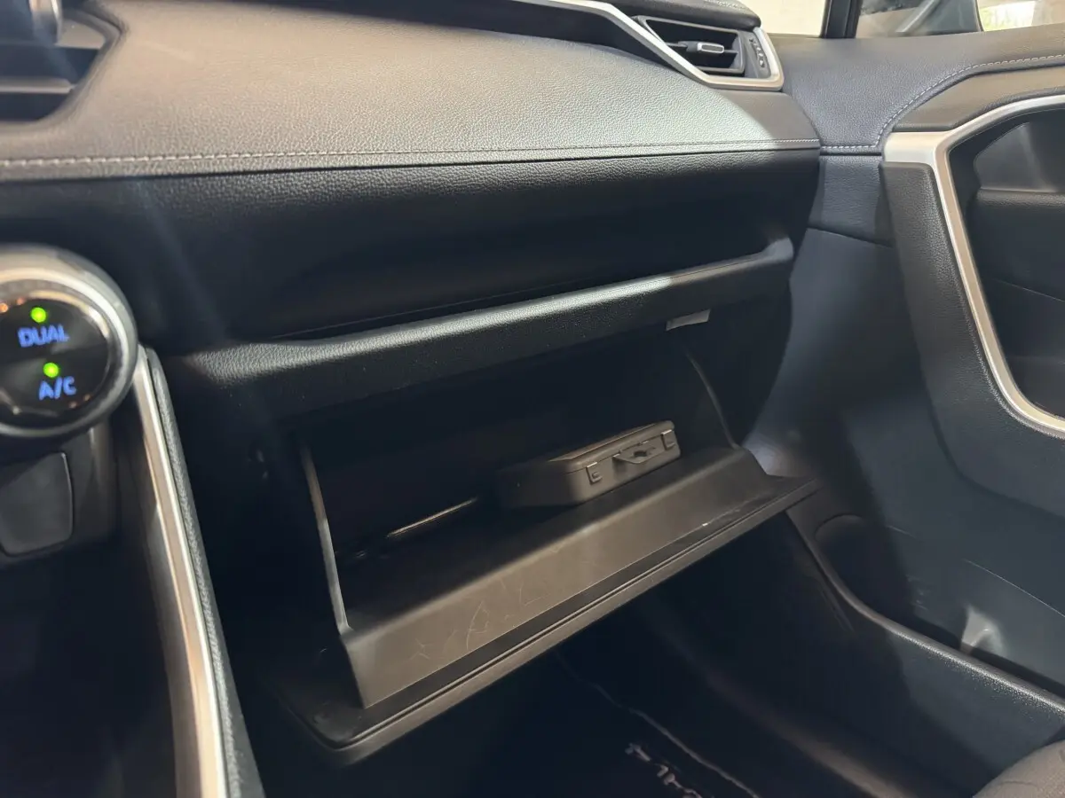 Gros plan sur la boîte à gants ouverte côté passager du Toyota RAV4 gris clair, montrant un boîtier électronique à l'intérieur.