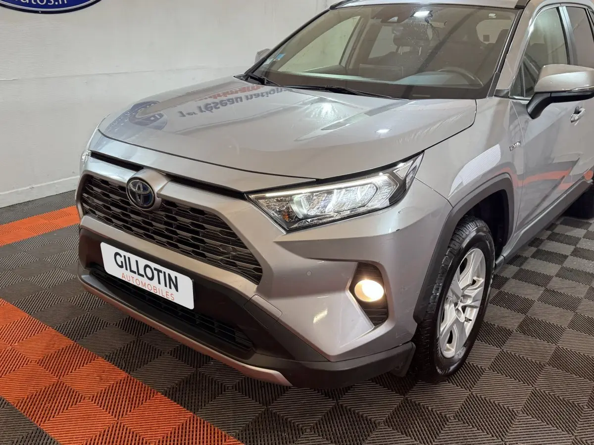 Vue 3/4 avant droit d'un Toyota RAV4 gris clair hybride avec phares LED et antibrouillards allumés.