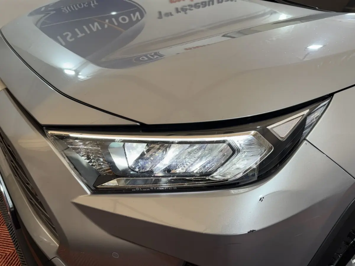 Gros plan sur le phare avant droit du Toyota RAV4 hybride gris clair, soulignant les lignes modernes et les LED distinctives.