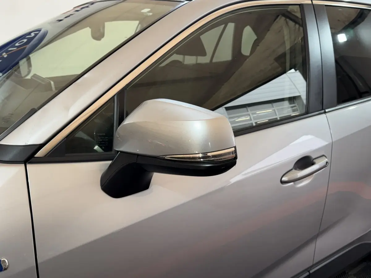 Rétroviseur côté gauche gris clair du Toyota RAV4 hybride 2021, avec poignée de porte visible en arrière-plan.