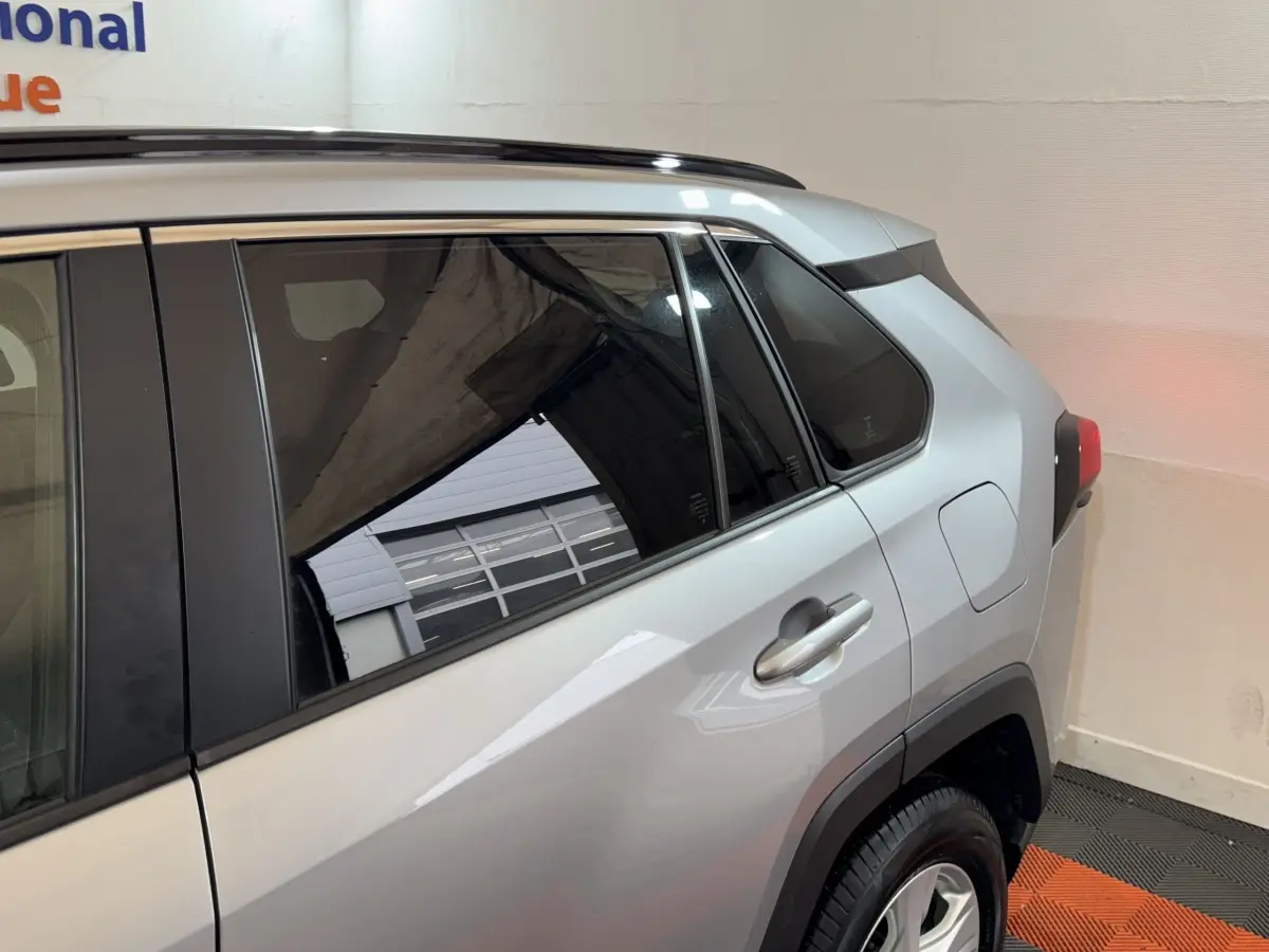 Vue côté arrière droit du Toyota RAV4 hybride gris clair, mettant en valeur la porte arrière et la roue.