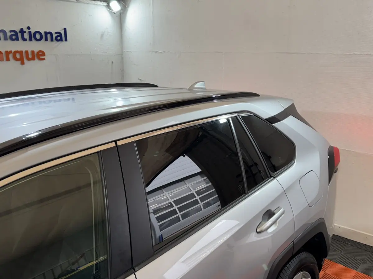 Vue latérale droite d'un Toyota RAV4 gris clair 2021 avec barres de toit noires et vitres teintées.