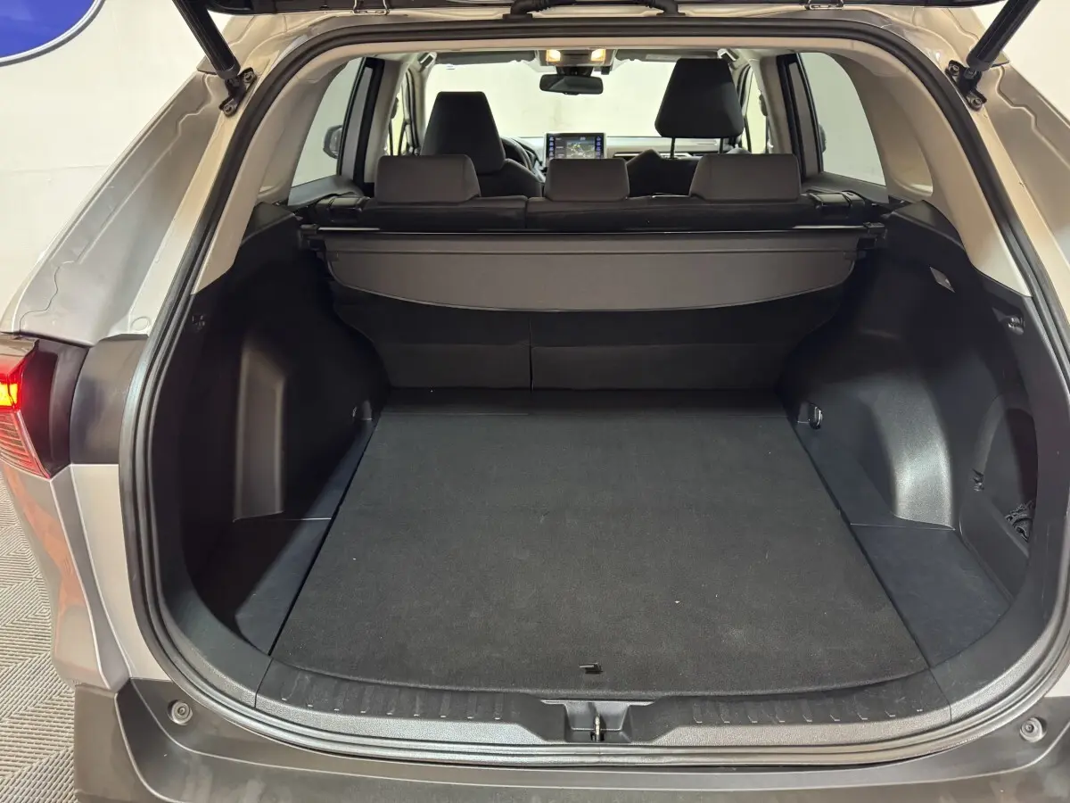 Coffre ouvert vu de l'arrière d'un Toyota RAV4 gris clair, montrant un espace de chargement spacieux avec cache-bagages.